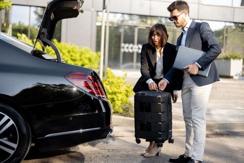 Two business professionals loading luggage into a HakuCab vehicle outside an office building.